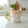 Keeyos PH handmade ceramic donut mug with pink glaze, colorful sprinkles, and a yellow swirl handle.