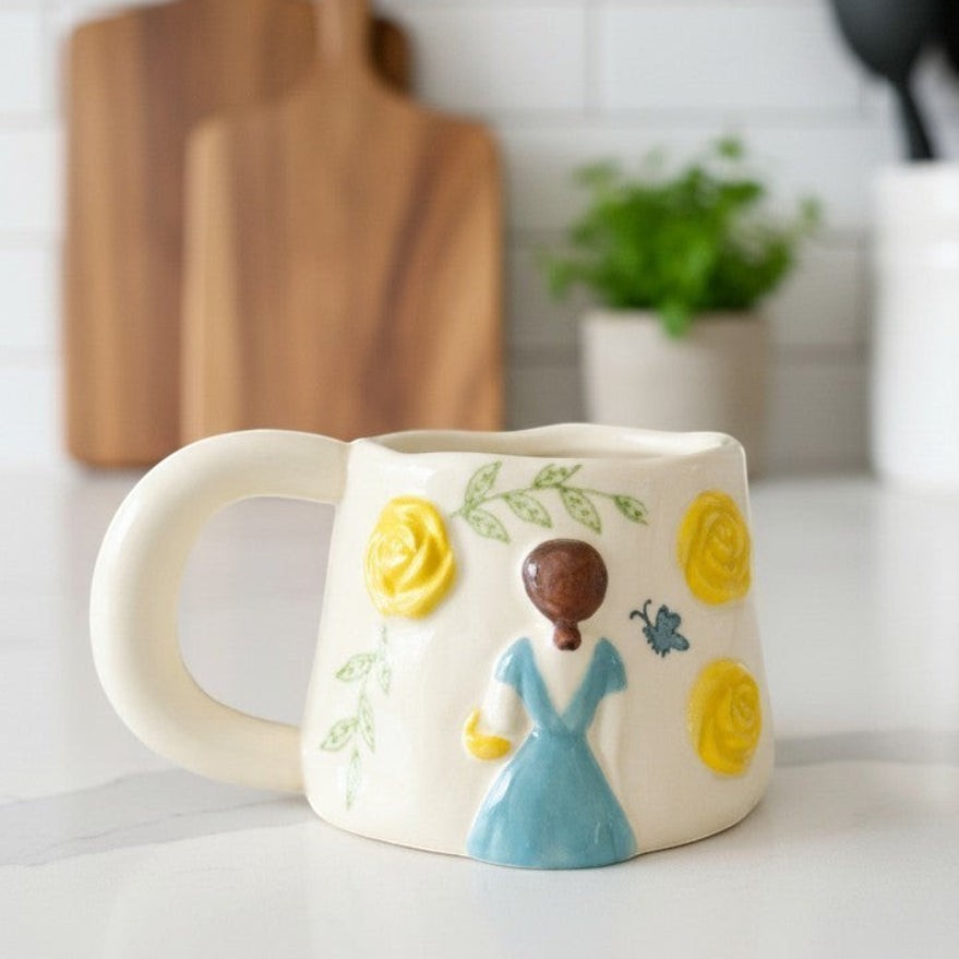 Keeyos PH cream ceramic mug with yellow roses, green leaves, and a blue dress figure with a butterfly.