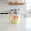Keeyos PH yellow ceramic mug with a pink bow and starry pattern, featuring a ruffled white rim.