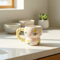 Keeyos PH hand-painted ceramic mug with yellow tulips and a puffy yellow handle. Pastel pink base with purple accents.